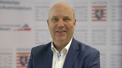 Michael Ashelm Michael Ashelm lächelt in die Kamera. Er ist bis zur Brust zu sehen, trägt ein blaugraues Sakko und ein weißes Hemd.
