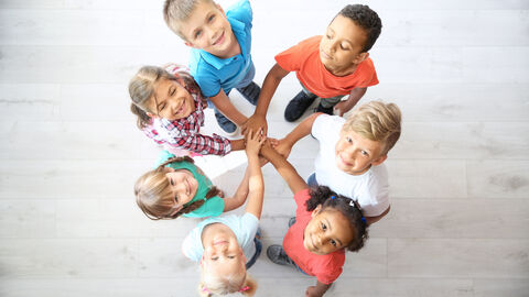 Mehrere Kinder stehen im Kreis und halten ihre Hände in der Mitte zwischen sich übereinander Mehrere Kinder stehen im Kreis und halten ihre Hände in der Mitte zwischen sich übereinander