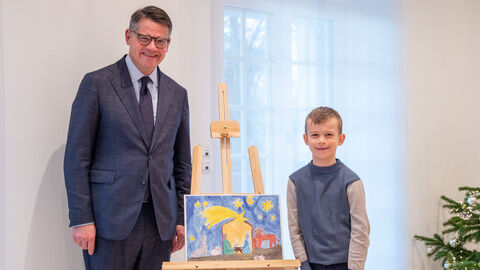 Erster Platz für dieses gemalte Bild! Der Ministerpräsident und der siebenjährige Richard stehen neben dem gemalten Siegerbild und lachen in die Kamera