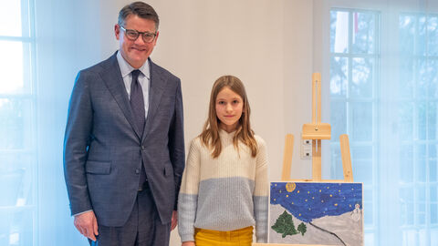 Zweiter Platz! Boris Rhein und die neunjährige Amelie stehen neben dem gemalten Winter-Bild, beide gucken in die Kamera