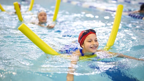 Hessen lernt Schwimmen Lachende Kinder im Hallenbad auf Schwimmnudeln
