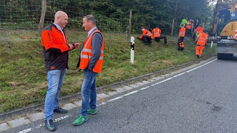 Landwirtschaftsminister Jung und sein Ministerkollege Peter Hauk stehen am Straßenrand. Im Hintergrund wird der Zaun von weiteren Personen errichtet.