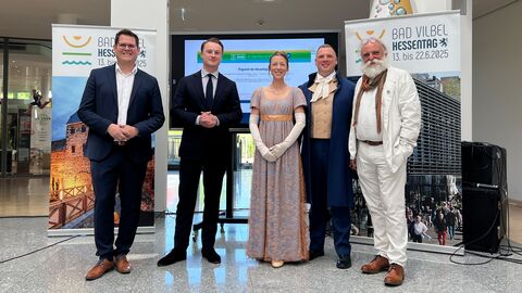 Eine Gruppe Personen steht zusammen vor Aufstellern des Hessentags in Bad Vilbel.