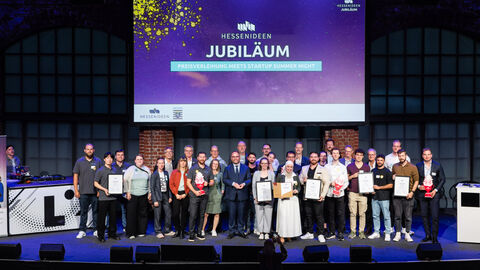 Wissenschaftsminister Timon Gremmels mit den Gewinnerteams des "Hessen Ideen"-Wettbewerbs 2025 Mehrere Personen stehen nebeneinander auf einer Bühne. Im Hintergrund wird auf eine Leinwand "Hessen Ideen Jubiläum" projiziert.