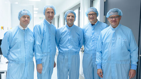 Ministerpräsident Boris Rhein bei der Eröffnung des neuen Reinraums der Firma Zeiss SMT in Roßdorf.  Fünf Personen stehen in blauen Schutzanzügen nebeneinander in einem hellen Raum.