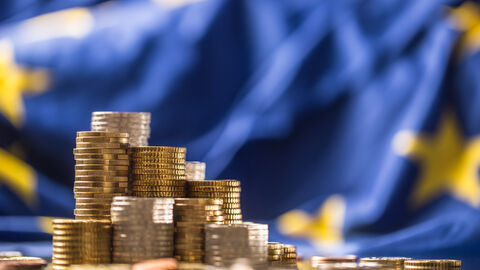 Geldmünzen vor Europaflagge Geldmünzenstapel vor Europaflagge