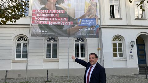 Alexander Lorz zeigt auf ein großes Plakat an einer Hauswand
