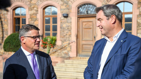 Ministerpräsident Rhein neben Markus Söder. Die beiden befinden sich im Gespräch und stehen vor einem Gebäude.