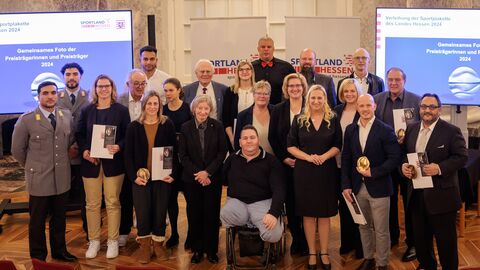 Über 15 Menschen stehen zusammen und schauen in die Kamera