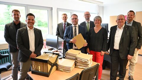 Diese Papierakten gehören der Vergangenheit an. Darüber freuen sich: Dominik Kaiser (Leiter Amt für Ausbildungsförderung Studierendenwerk Gießen), Gero Lottermann (Geschäftsführer Studierendenwerk Gießen), Wolfgang Rettich (Geschäftsführer Studierendenwerk Darmstadt), Timon Gremmels (Hessischer Minister für Wissenschaft und Forschung, Kunst und Kultur), Johannes Tiebel (Stv. Geschäftsführer Studierendenwerk Frankfurt), Christa Ambrosius (Geschäftsführerin Studierendenwerk Kassel), Dr. Uwe Grebe (Geschäftsführer Studierendenwerk Marburg), Ben Kopfer (Leiter Amt für Ausbildungsförderung Studierendenwerk Darmstadt).  Wissenschaftsminister Timon Gremmels mit weiteren Personen stehen hinter einem Tisch mit Papierakten