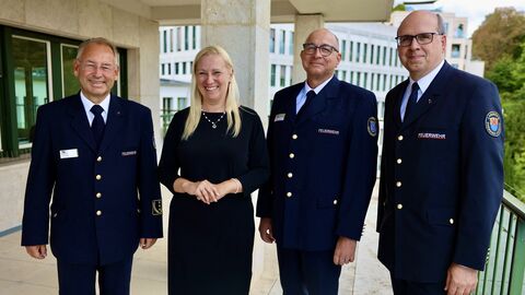 Gesundheitsministerin Stolz steht mit 3 Männern in Uniform zusammen und lächelt in Kamera.