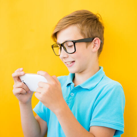 Das liest sich gut! Junge vor einer gelben Wand schaut lachend auf sein Smartphone